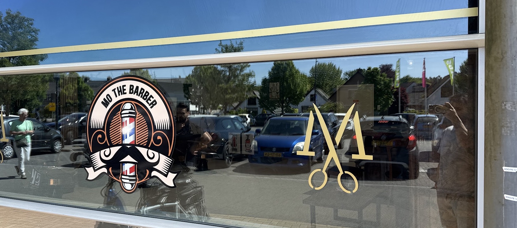 De etalage van Mo The Barbershop aan de Smidsweg in Nijverdal, met het logo en een gouden schaar op het glas
