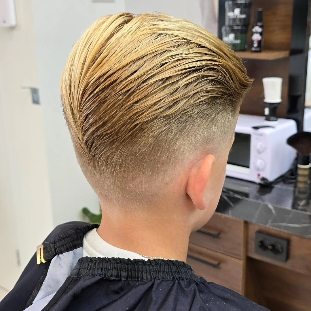Een afgewerkte blonde fade met slick-back, van achteren gezien in de barbershop